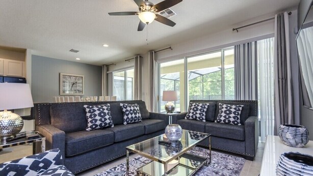 A modern living room with a dark grey sofa, a glass coffee table, and a ceiling fan. - 8 Bedroom 5 Bathroom Bella Vida Resort 498mb (Kissimmee)
