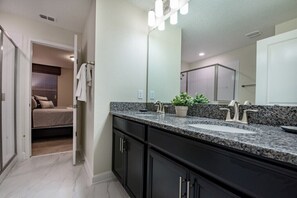 A modern bathroom with a granite countertop, a large mirror, and a shower area visible through a glass door.
