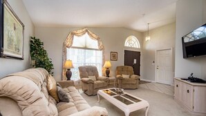 A living room with a beige sofa, two armchairs, a coffee table, and a television.
