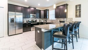 A modern kitchen with dark cabinets, stainless steel appliances, a granite island, and bar stools.