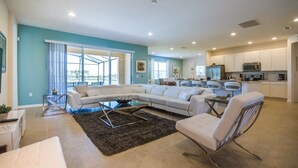 A spacious living room with a sectional sofa, a glass coffee table, and a black rug. The kitchen area is visible with white cabinets and modern appliances. - Broad Oak Villa Solaterra (Davenport)