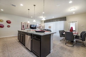 Una cocina moderna con una isla central, comedor con sillas y televisor en la pared.