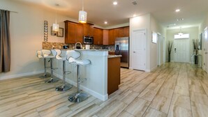 A modern kitchen with a central island, bar stools, stainless steel appliances, and a stone backsplash. - Ultimate Champions Gate Resort 8 Bedroom 5 Bath (Davenport)