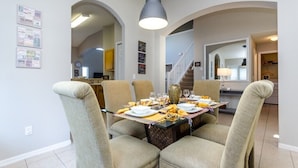 Un coin repas avec une table dressée pour quatre personnes, des chaises de couleur beige et un luminaire suspendu.