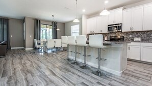 A modern kitchen with white cabinets, a granite countertop, and a central island with bar stools. - 6 Bedroom 5 Bathroom in Solterra Resort 5425sc (Davenport)