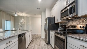 Una cocina moderna con encimeras de granito, electrodomésticos de acero inoxidable y una salpicadera de azulejos pequeños.