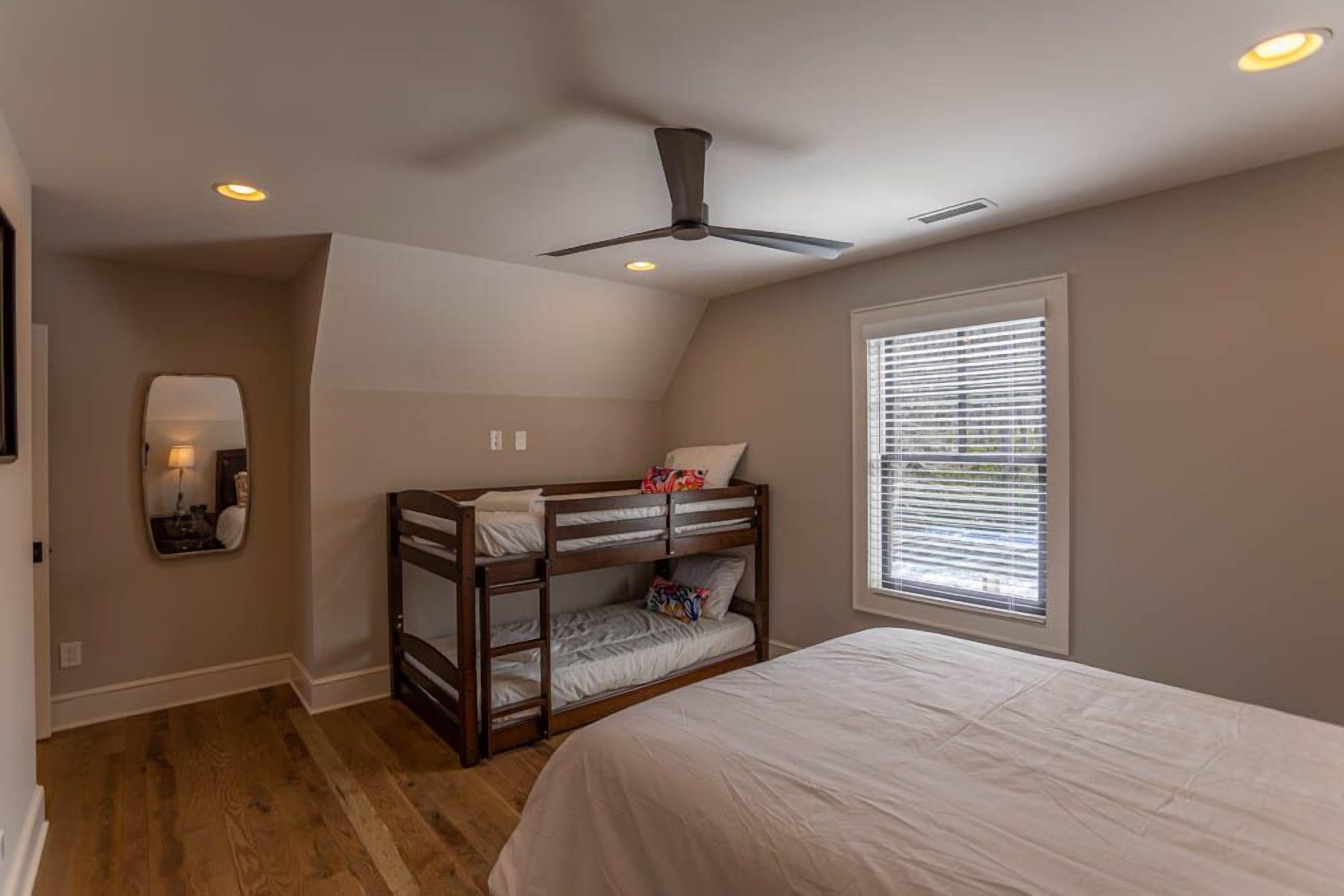 Une chambre avec un lit superposé, un ventilateur de plafond, une fenêtre avec des stores et un plancher en bois.