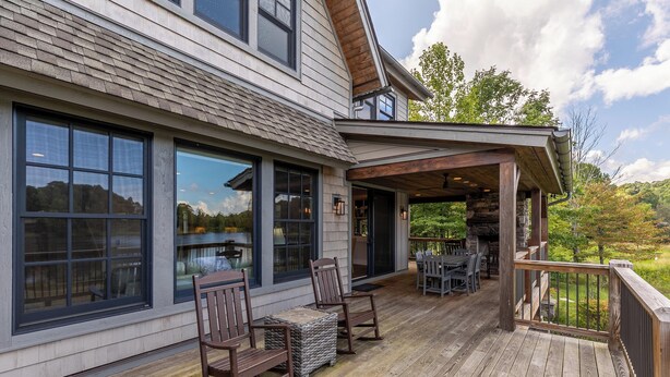 A wooden deck with outdoor furniture, large windows, and a stone fireplace. - Lakeshore Retreat- new construction in Sweetgrass, right on the lake (Blowing Rock)