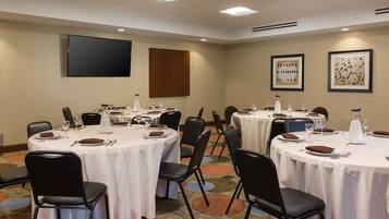 A conference room with round tables, black chairs, and white tablecloths.