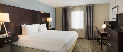 Habitación de hotel con una cama grande, dos mesitas de noche con lámparas, un escritorio con silla y un televisor.