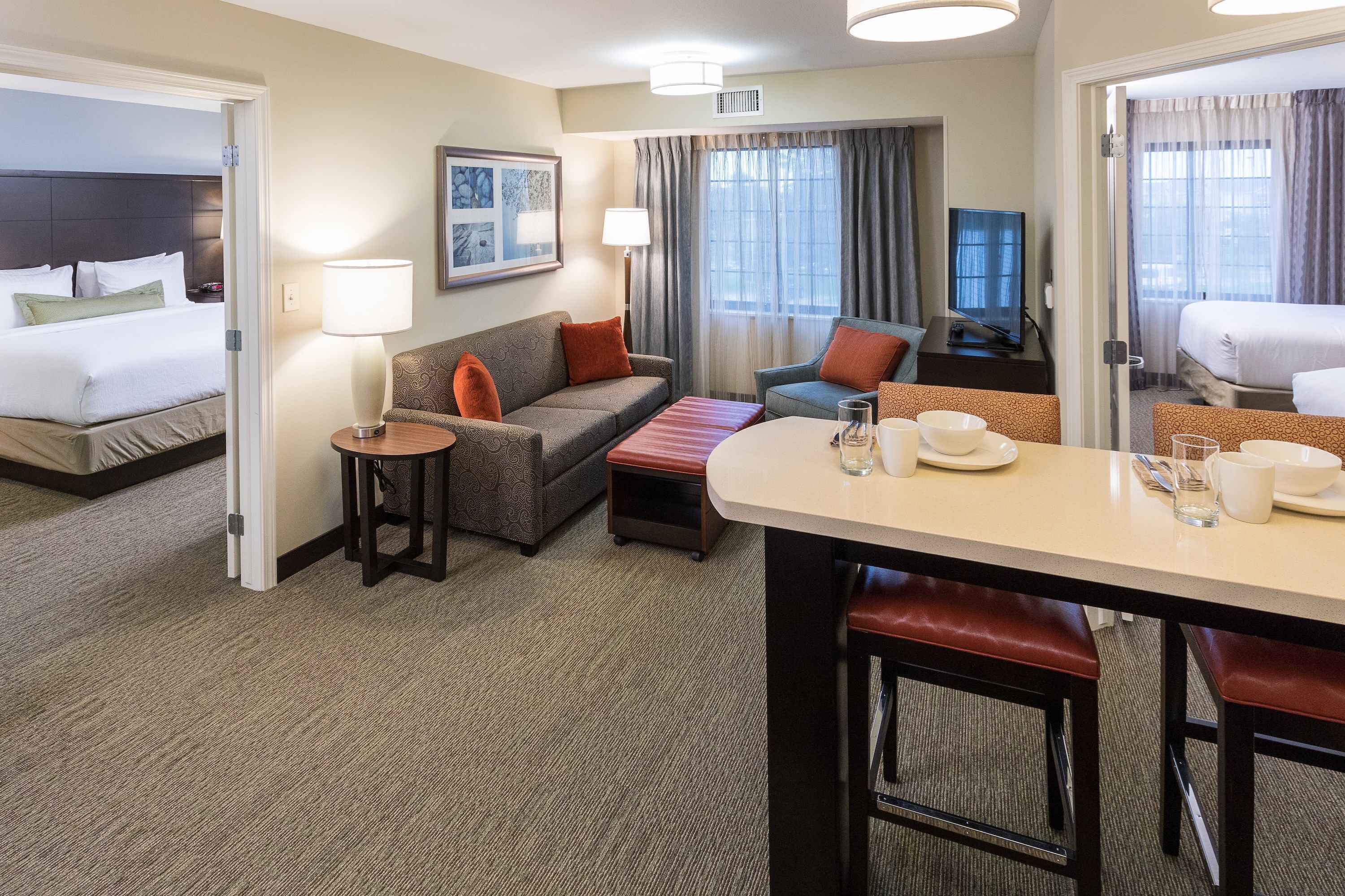 A hotel room with a bed, a sofa, a dining table with chairs, a TV, and a window with curtains.