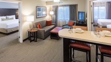 A hotel room with a bed, a sofa, a dining table with chairs, a TV, and a window with curtains.