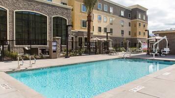 A swimming pool with a stone facade, palm trees, and outdoor seating.