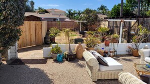 A patio area with outdoor furniture, potted plants, and a wooden fence. - The Williams Cottage (Carlsbad)