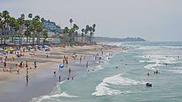 A beach with people swimming and walking along the shore. - The Williams Cottage (Carlsbad)