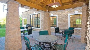 Un patio al aire libre con muros de piedra, una mesa redonda y sillas verdes.