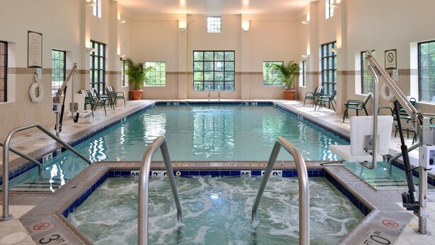 Una amplia piscina interior con agua cristalina, rodeada de sillones de descanso y plantas en macetas.