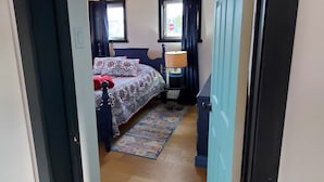 Ein Schlafzimmer mit einem Bett, einem Nachttisch, einer Lampe und einem Fenster mit Vorhängen.