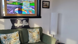 Ein grünes Sofa mit floralen Kissen, ein gerahmtes abstraktes Gemälde und ein kleiner Tisch mit einer Fernbedienung.