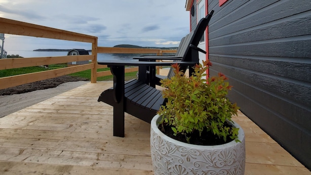 Eine Holzterrasse mit einer schwarzen Bank und einem weißen Pflanzgefäß mit grünen Pflanzen.