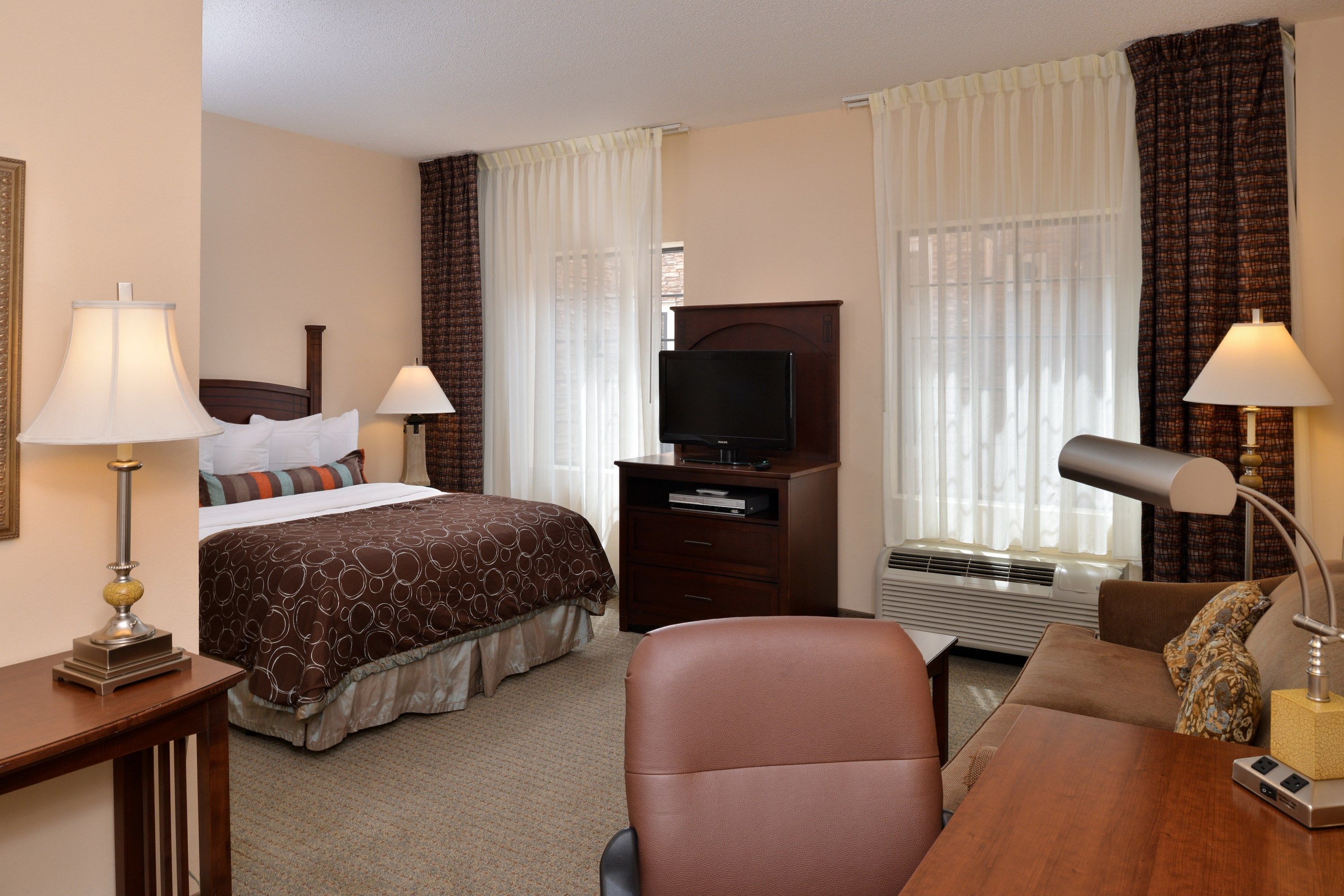 Une chambre d’hôtel équipée d’un lit, d’un bureau, d’une chaise, d’une télévision et d’une lampe de bureau.