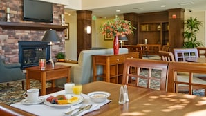 Een hotel lobby met een open haard, een zithoek en een ontbijtbuffet.