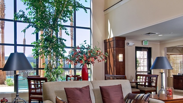 A spacious lobby with a large window, a chandelier, a sofa, a coffee table, and a plant. - Accessible King Suite w/ Bathtub in Palmdale (Palmdale)