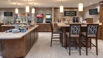 Une cuisine moderne dotée d’un bar pour prendre le petit-déjeuner, d’un distributeur de Coca-Cola et d’un panneau indiquant que le petit-déjeuner est offert gratuitement chaque jour.