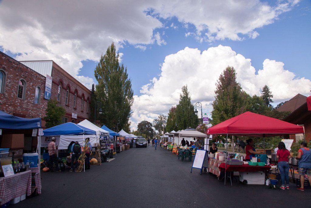 A street market with tents and tables, brick buildings, and trees.