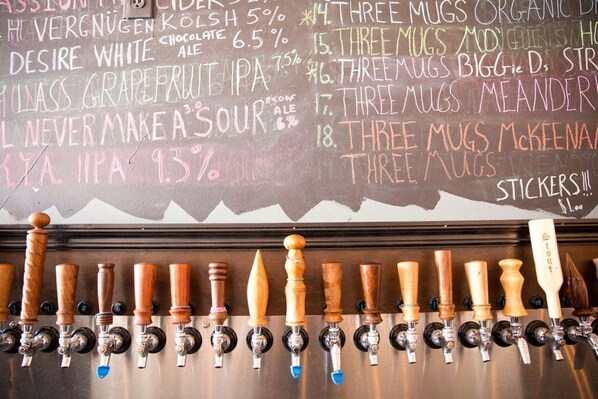 A bar area with a chalkboard menu listing various beer options and prices, and a row of taps with wooden handles.