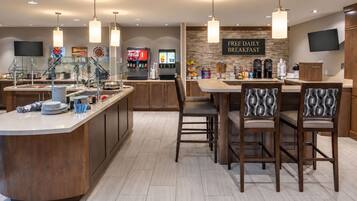 A modern kitchen with a breakfast bar, a Coca-Cola dispenser, and a sign offering free daily breakfast.