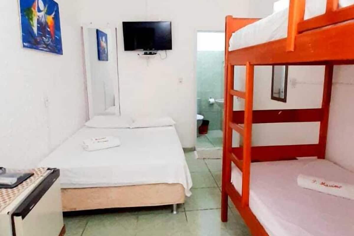Quarto de hotel pequeno e compacto, com uma cama de solteiro, uma escrivaninha e uma TV fixada na parede.