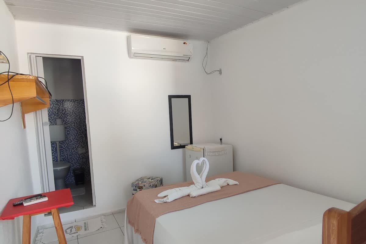 Quarto com cama, mesa de cabeceira, espelho e ar condicionado.