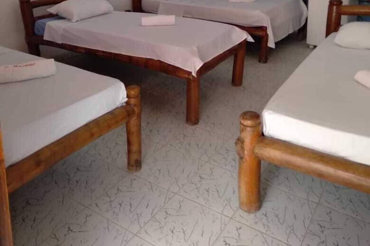 Quarto com três camas de madeira, parede azul com pintinhas brancas, ventilador de teto branco e um quadro de uma cena de praia.