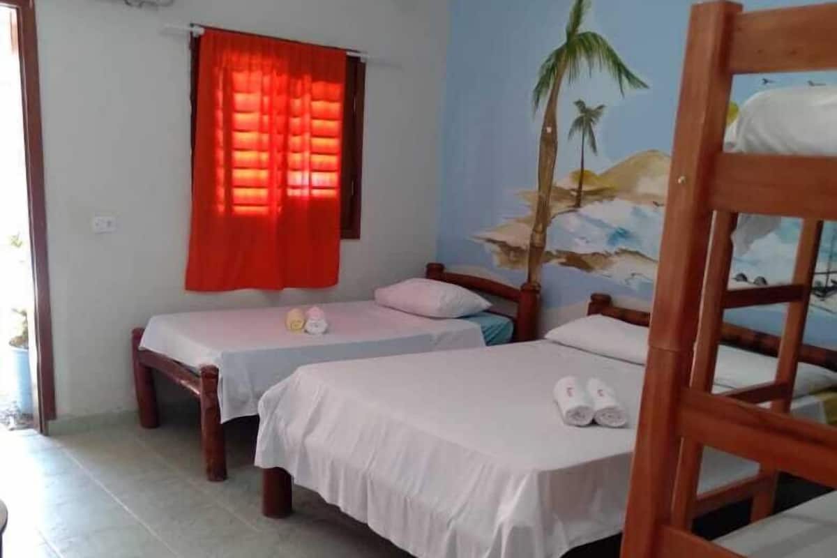 Quarto com duas camas de solteiro, uma cama beliche, uma cortina vermelha, um mural na parede e um aparelho de ar condicionado.