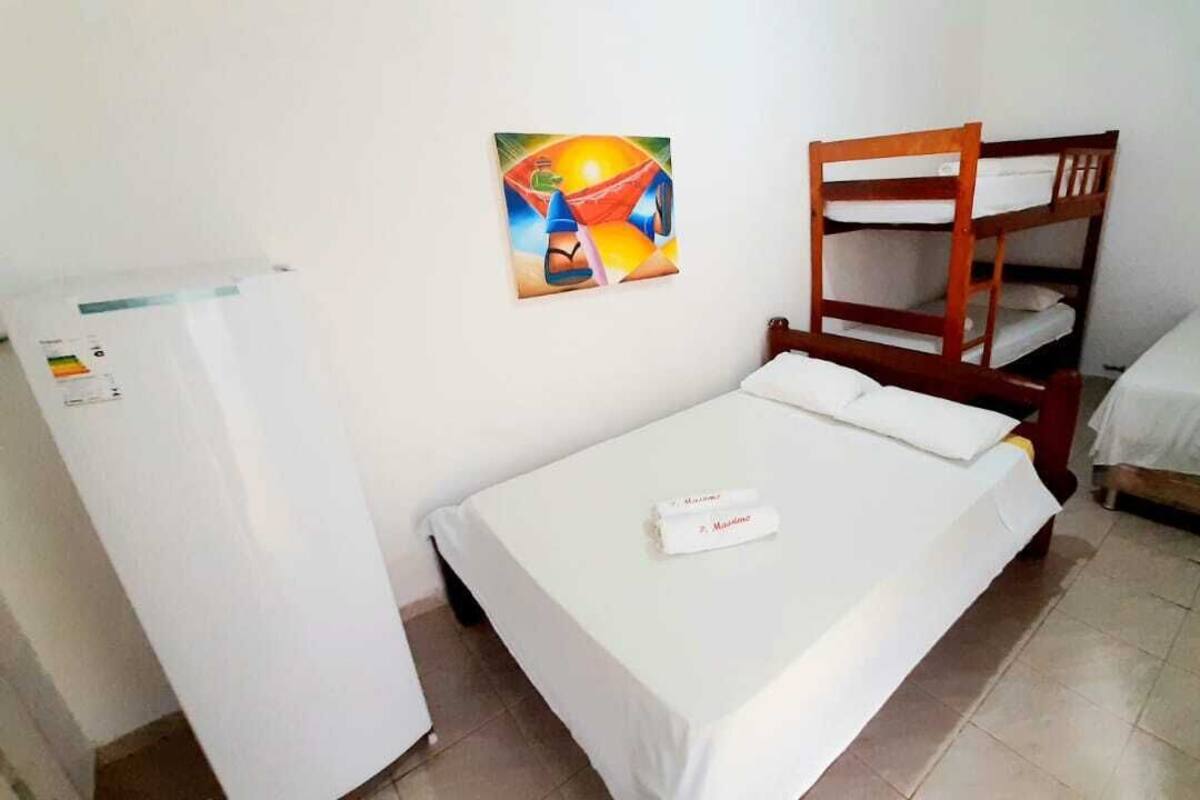 Quarto pequeno e limpo com beliche, cama individual, frigorífico e um quadro na parede.