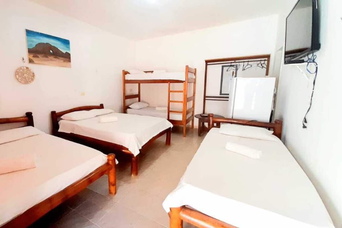 Quarto com três camas de madeira, uma mesa pequena, uma TV e um quadro na parede.