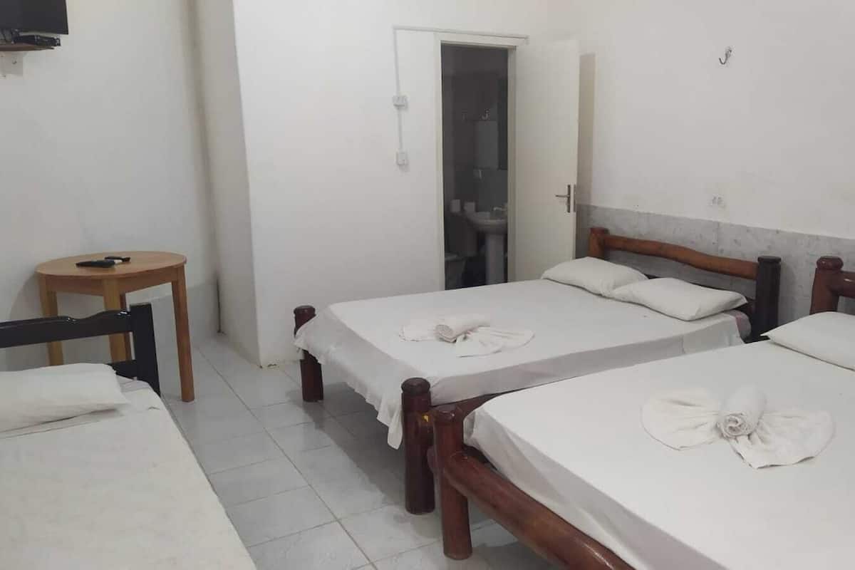Quarto de hotel com duas camas de solteiro, uma mesa pequena e uma televisão na parede.