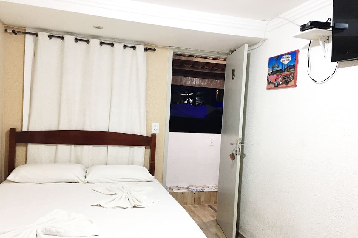 Quarto com cama, porta e televisão fixada na parede.