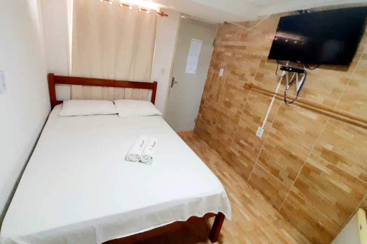 Uma cama de solteiro com cabeceira de madeira, televisão de tela plana na parede e piso de madeira.