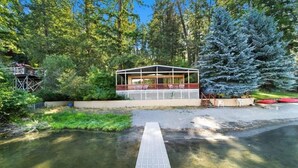 Una baita con veranda che si affaccia su un fiume, circondata da alberi.