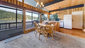 Una baita in legno con zona pranzo, cucina e ampie finestre che si affacciano su una zona boschiva.