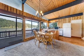 A wooden cabin with a dining area, kitchen, and large windows overlooking a forested area. - Waterfront Cabin w/ Private Beach & Dock (Kootenai County)