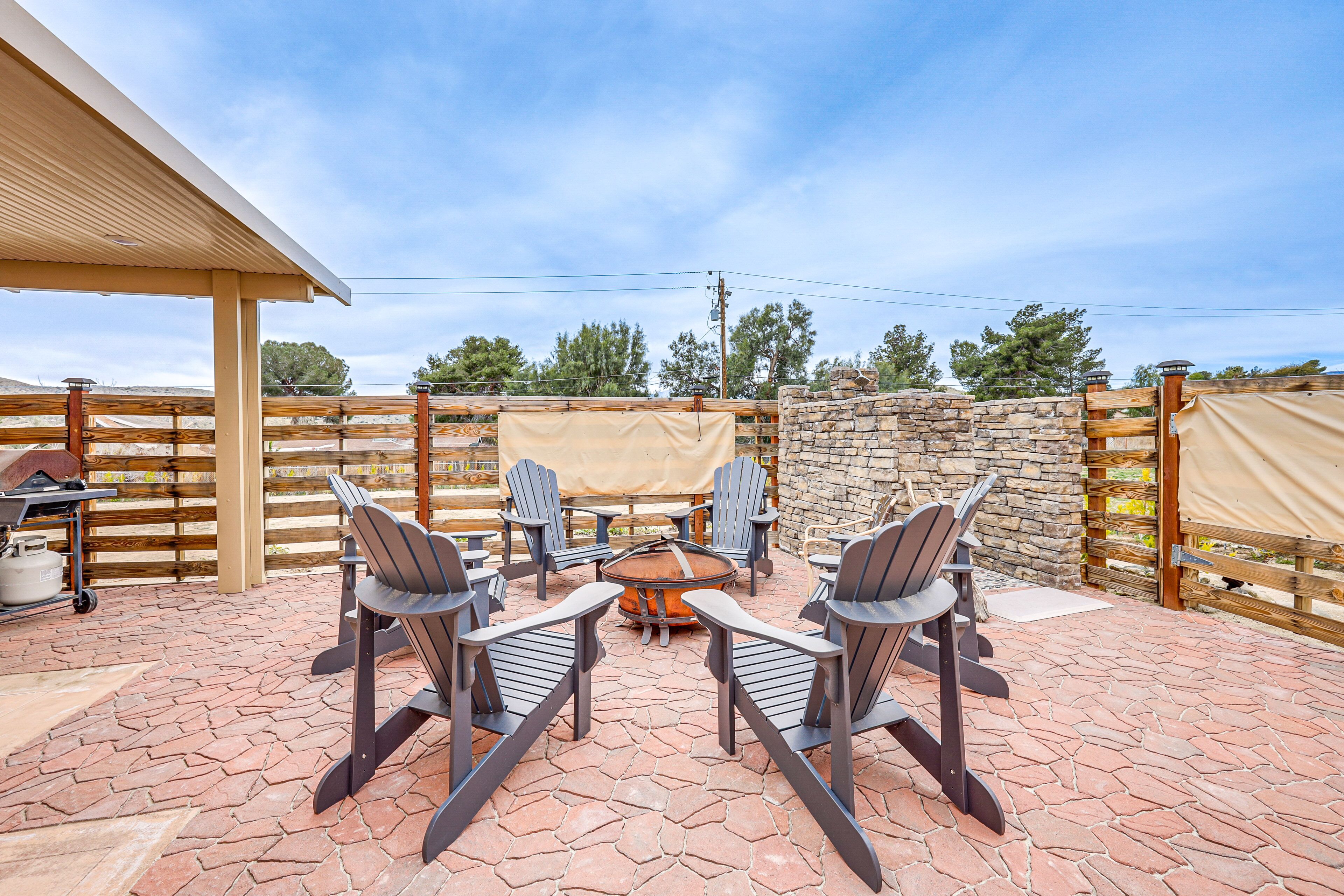 An outdoor patio with a stone floor, a round fire pit, and four Adirondack chairs.