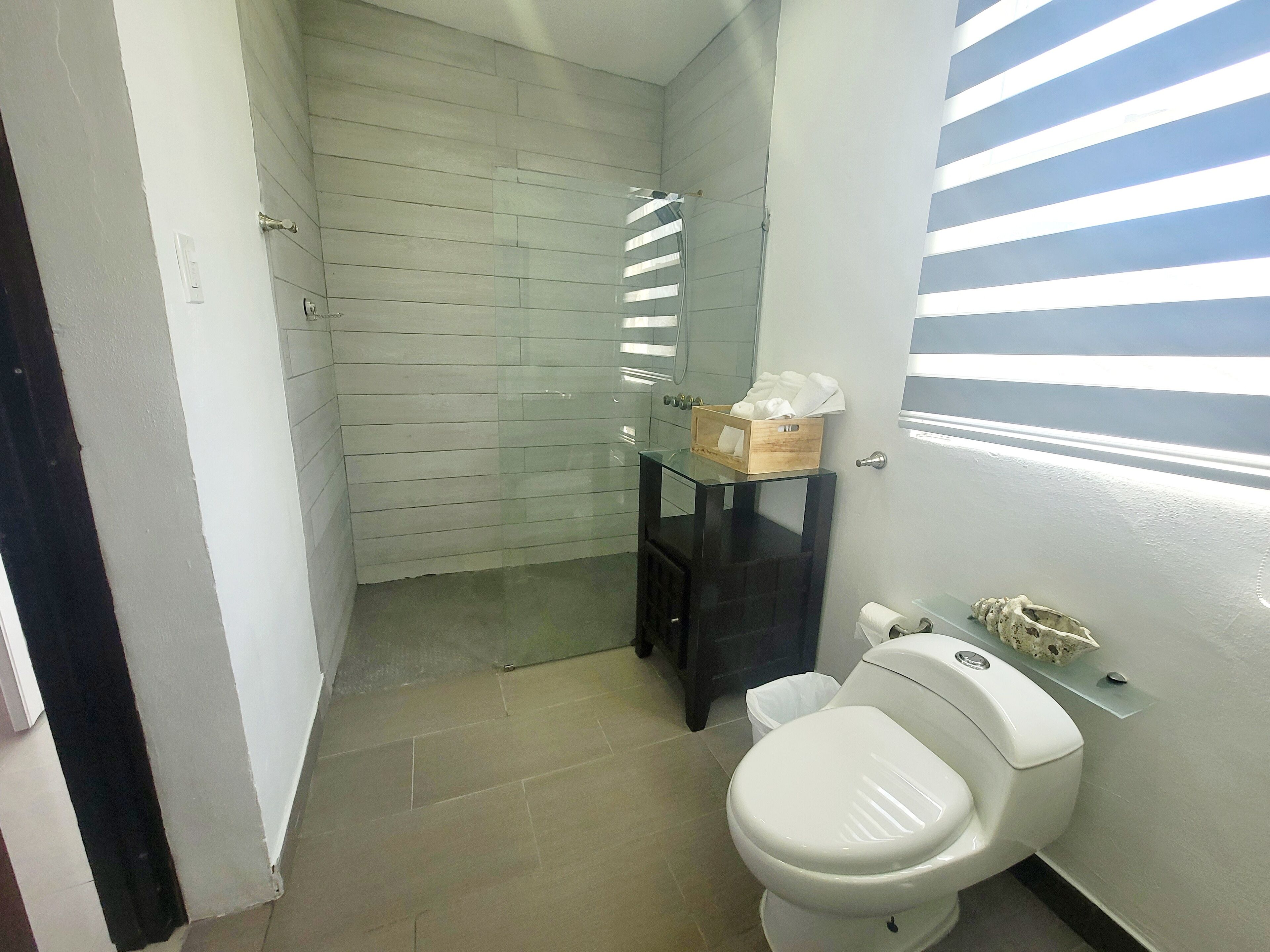 A bathroom with a white toilet, a glass shower enclosure, and a wooden box on a black shelf.