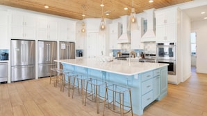 Una cucina moderna con mobili bianchi, elettrodomestici in acciaio inossidabile, una grande isola con sgabelli e soffitto in legno.