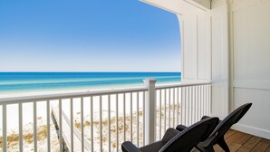 Vista sulla spiaggia da un portico con ringhiere bianche e due sedie in vimini.