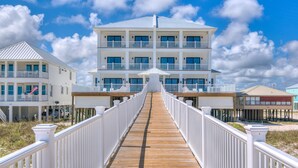 Een meerhoog hotel met een houten looppad naar de ingang, witte leuningen en een helderblauwe lucht.
