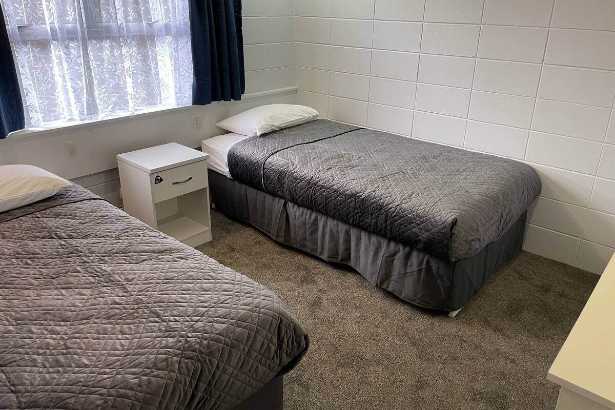Una habitación con dos camas, una mesita de noche blanca y una ventana con cortinas.