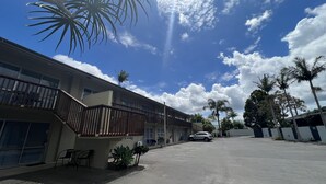 A multi-story motel with a balcony, a parking lot, and palm trees.